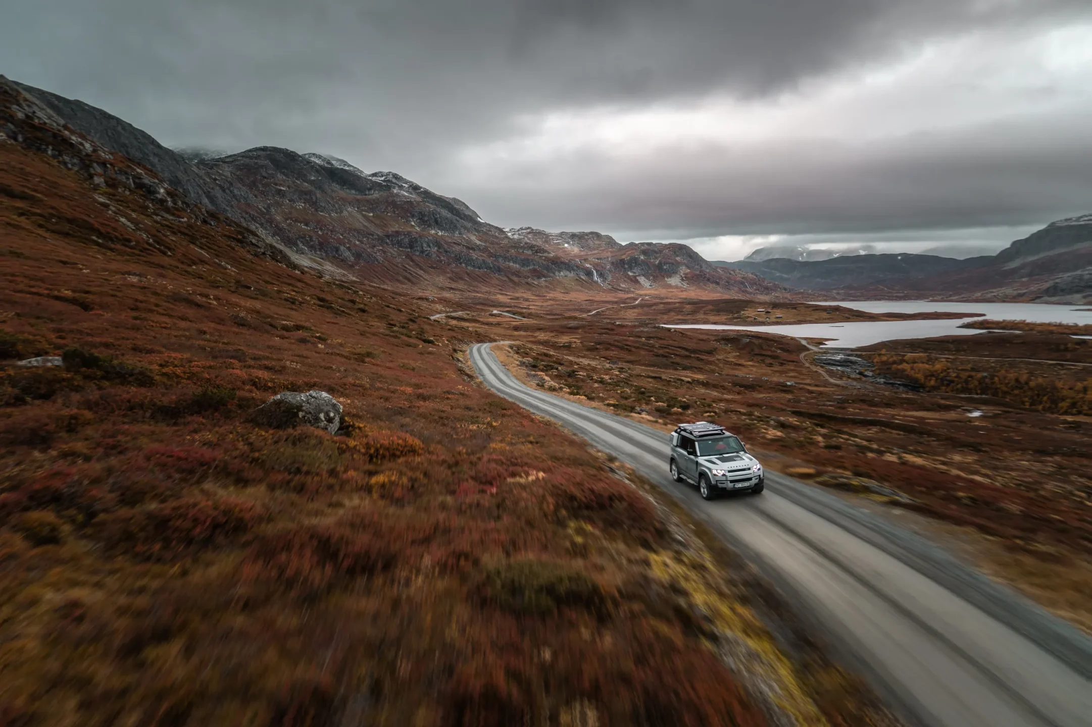 Bil på smal fjellvei gjennom norsk høyfjellslandskap under dramatisk himmel